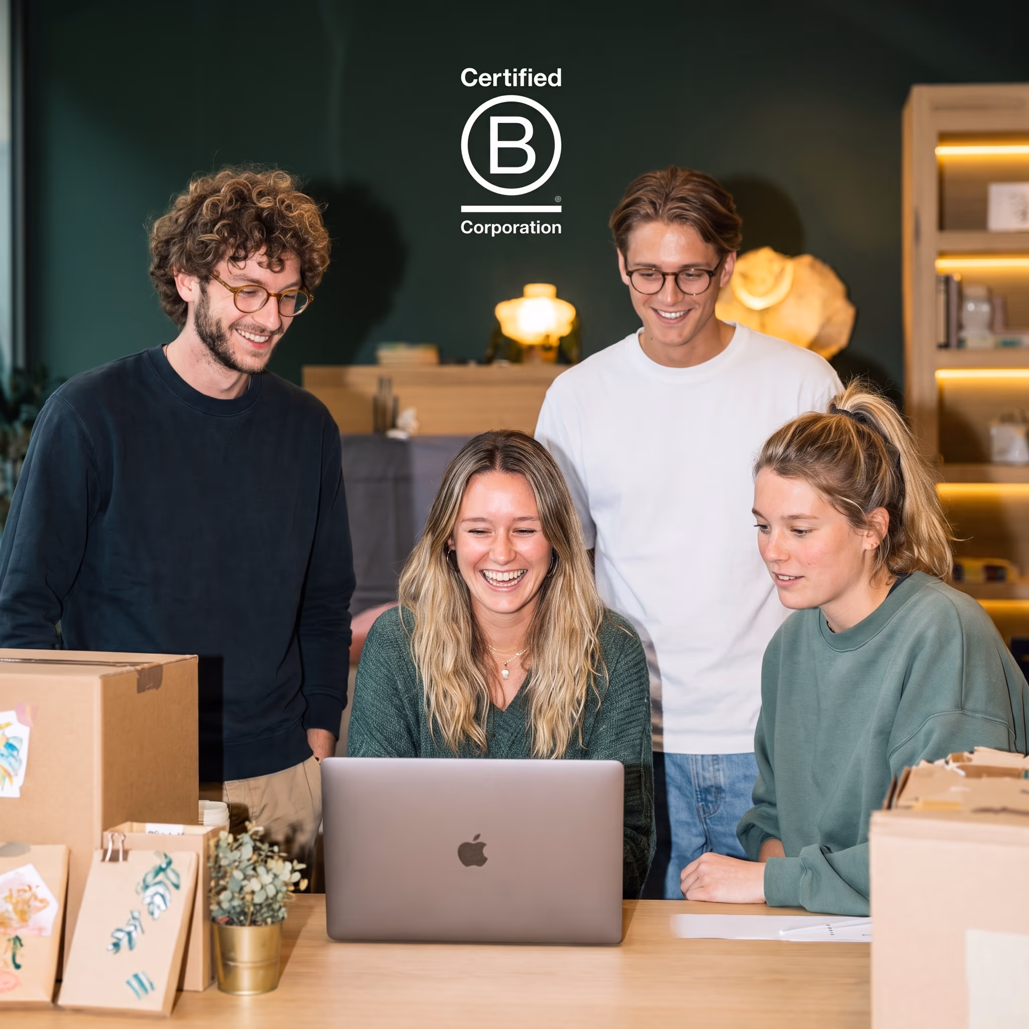 Quatre jeunes entrepreneurs souriants travaillent ensemble sur un ordinateur portable, entourés de cartons d'expédition