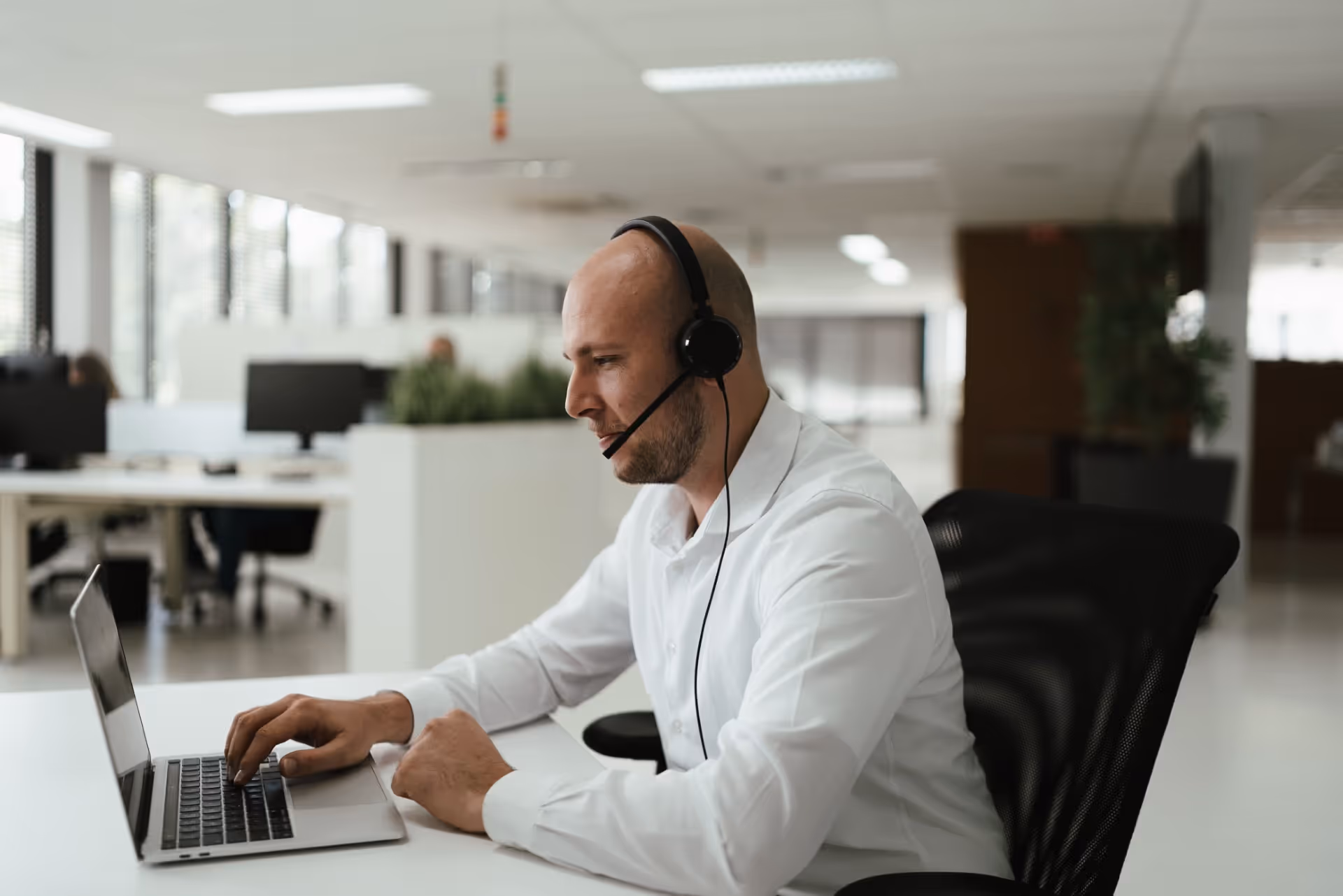 Support agent with a headset answers questions behind his laptop